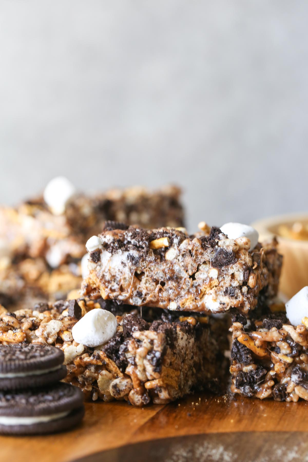Close up shot of three cut S'more Bars stacked on a wood cutting board with two whole Oreo cookies stacked next to them. 