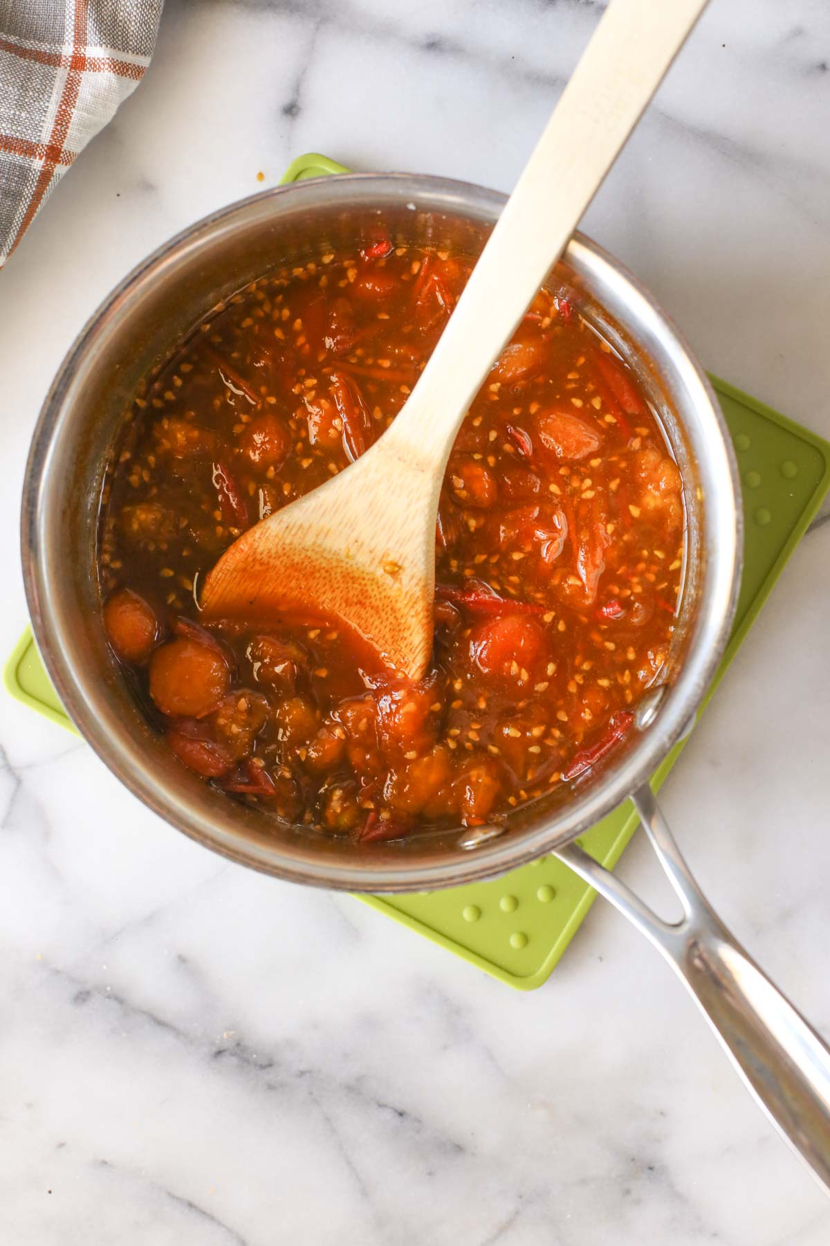 Overhead shot of Tomato Jam in a saucepan during the cooking process with a wooden spoon in it.  