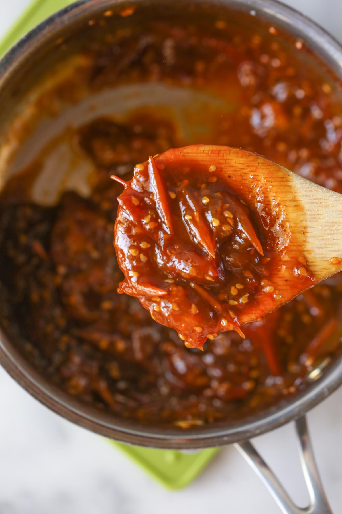Close up overhead shot of Tomato Jam on a wooden spoon after it has reduced, with the saucepan of Tomato Jam in the background.  
