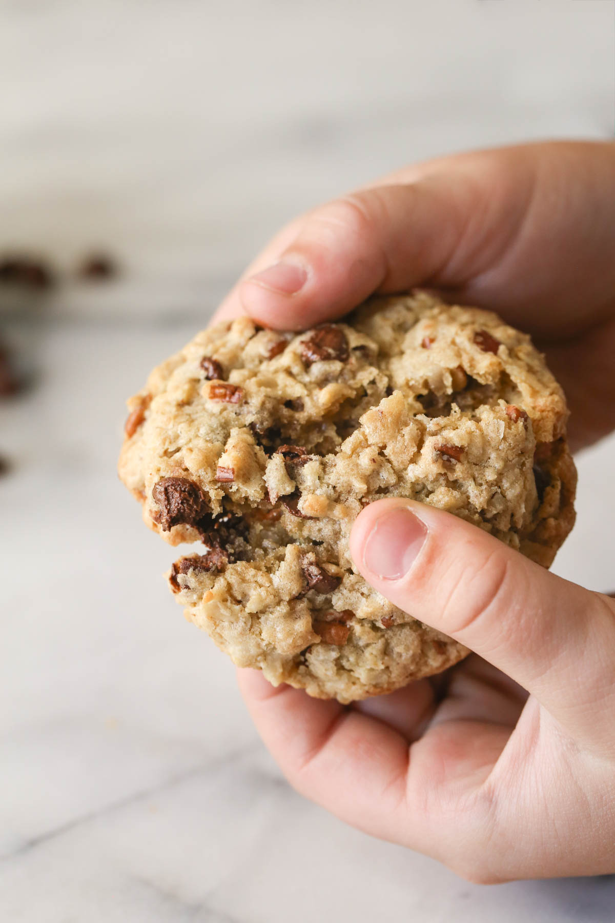 Close up shot of a hand breaking a Cowboy Cookie in half.