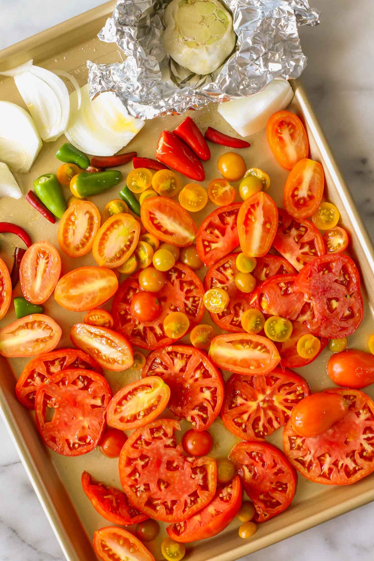 Overhead shot of tomatoes, peppers, onions, and garlic on a sheet pan, all ingredients for Roasted Tomato Salsa.
