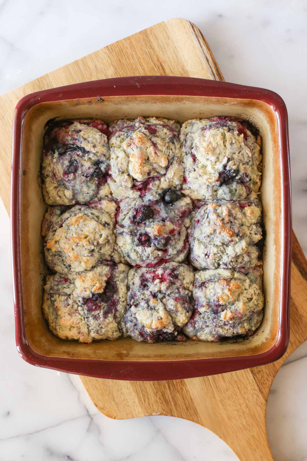 Overhead shot of a baking pan of Glazed Berry Drop Biscuits without the glaze, sitting on a wood cutting board.