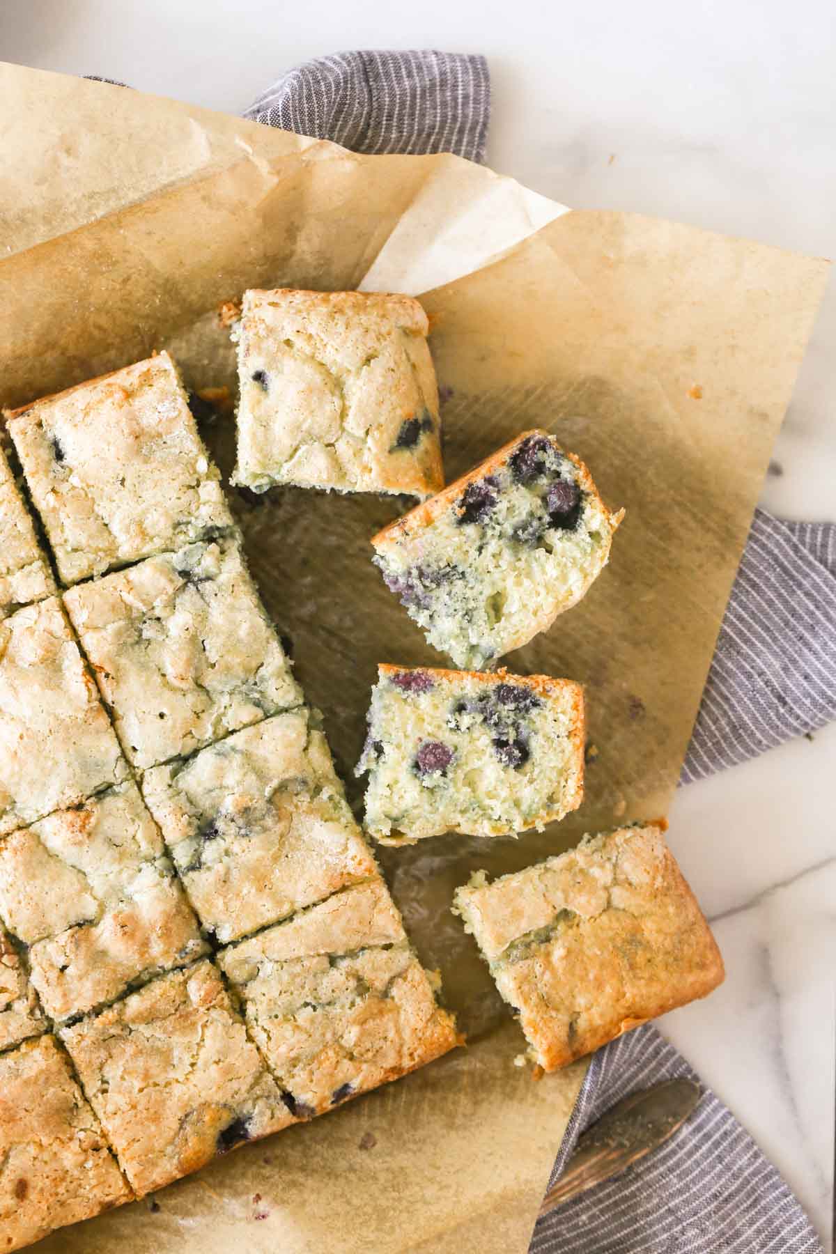 Overhead shot of Sourdough Blueberry Breakfast Cake on parchment paper that has been sliced into pieces.  