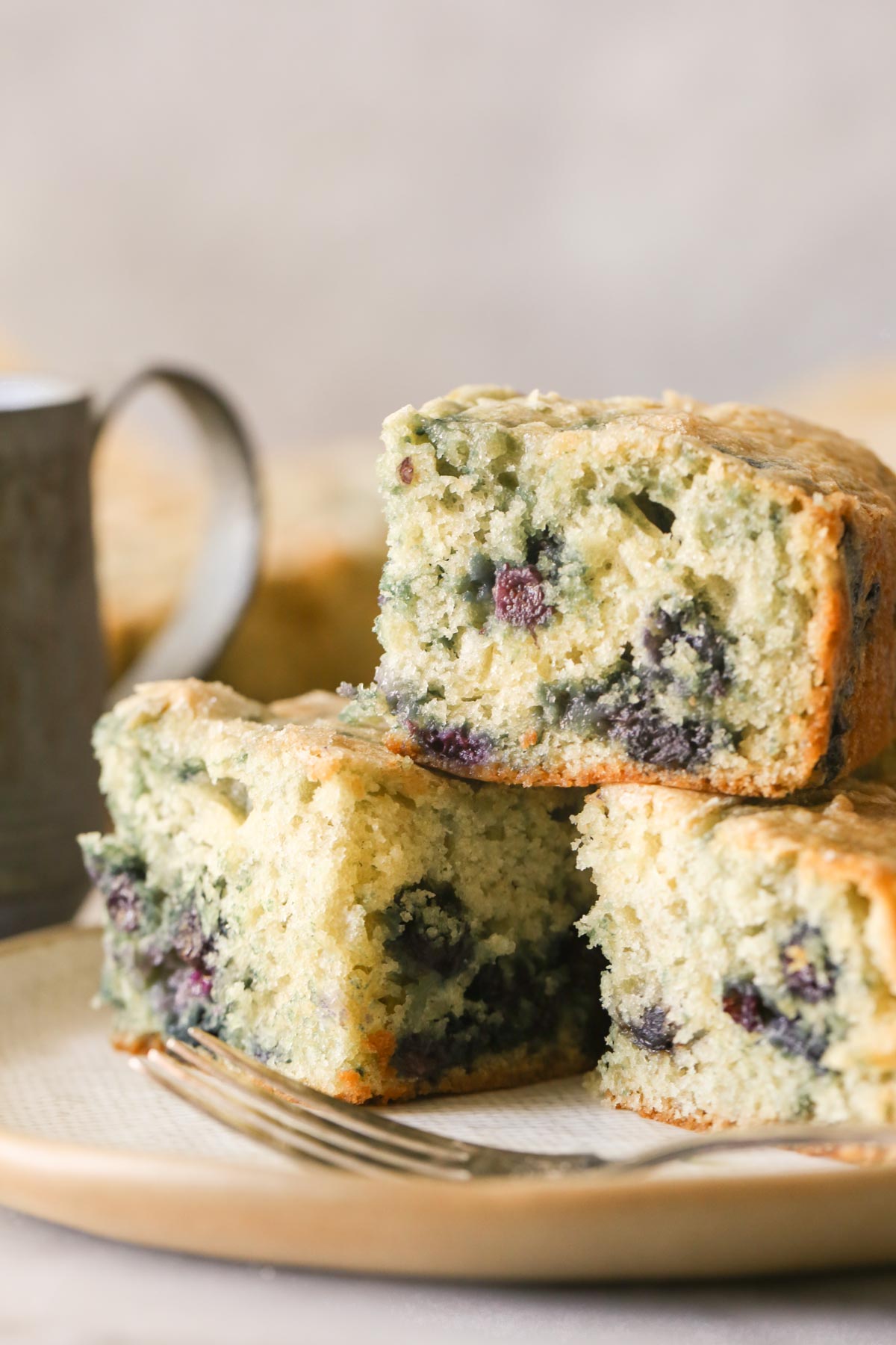 Close up shot of three pieces of Sourdough Blueberry Breakfast Cake stacked on a plate with a fork.  