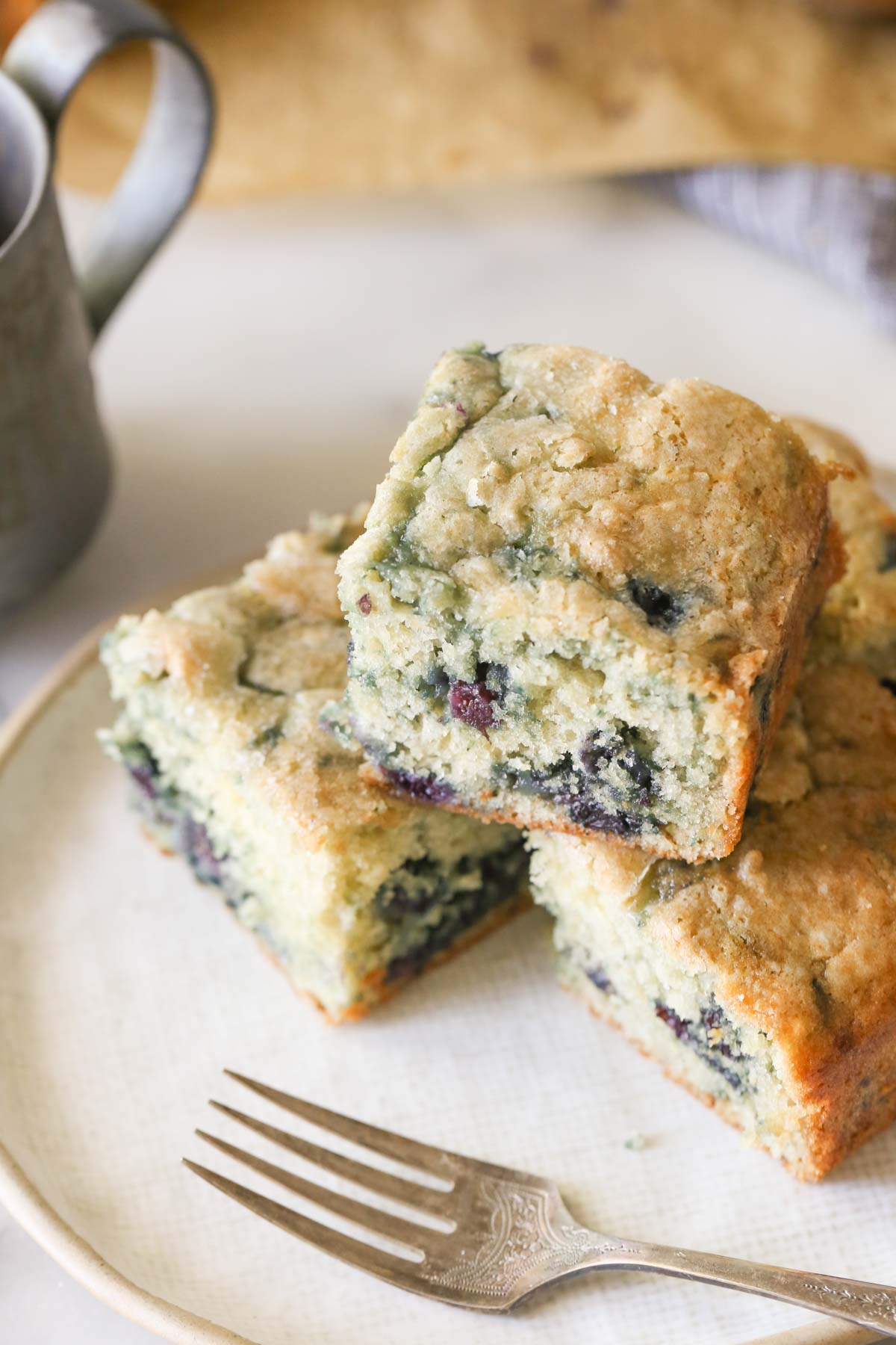 Overhead shot of four pieces of Sourdough Blueberry Breakfast Cake stacked on a plate with a fork.  