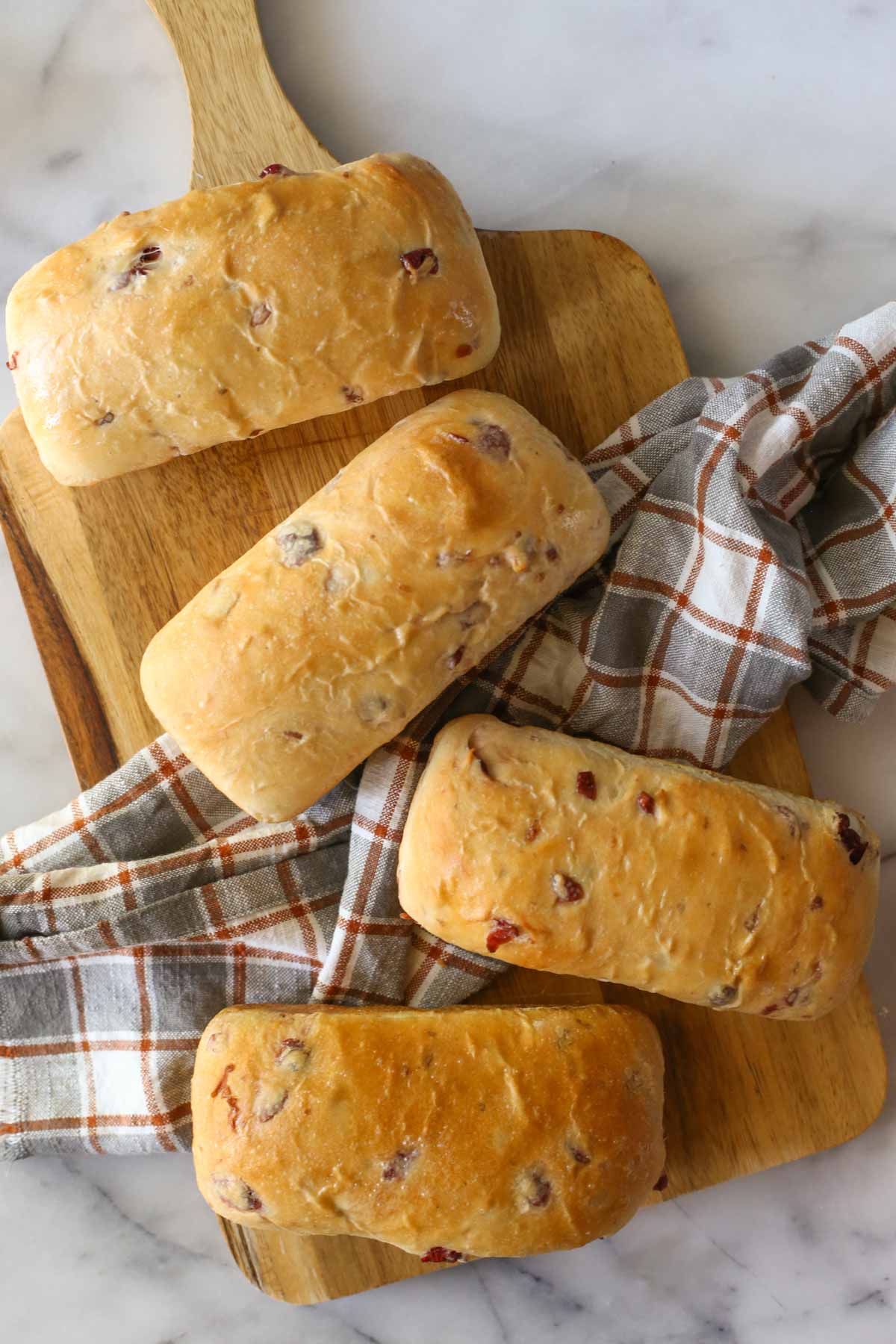 Overhead shot of four mini loaves of Sourdough Cranberry Bread on a wood cutting board, along with a plaid dish towel.  