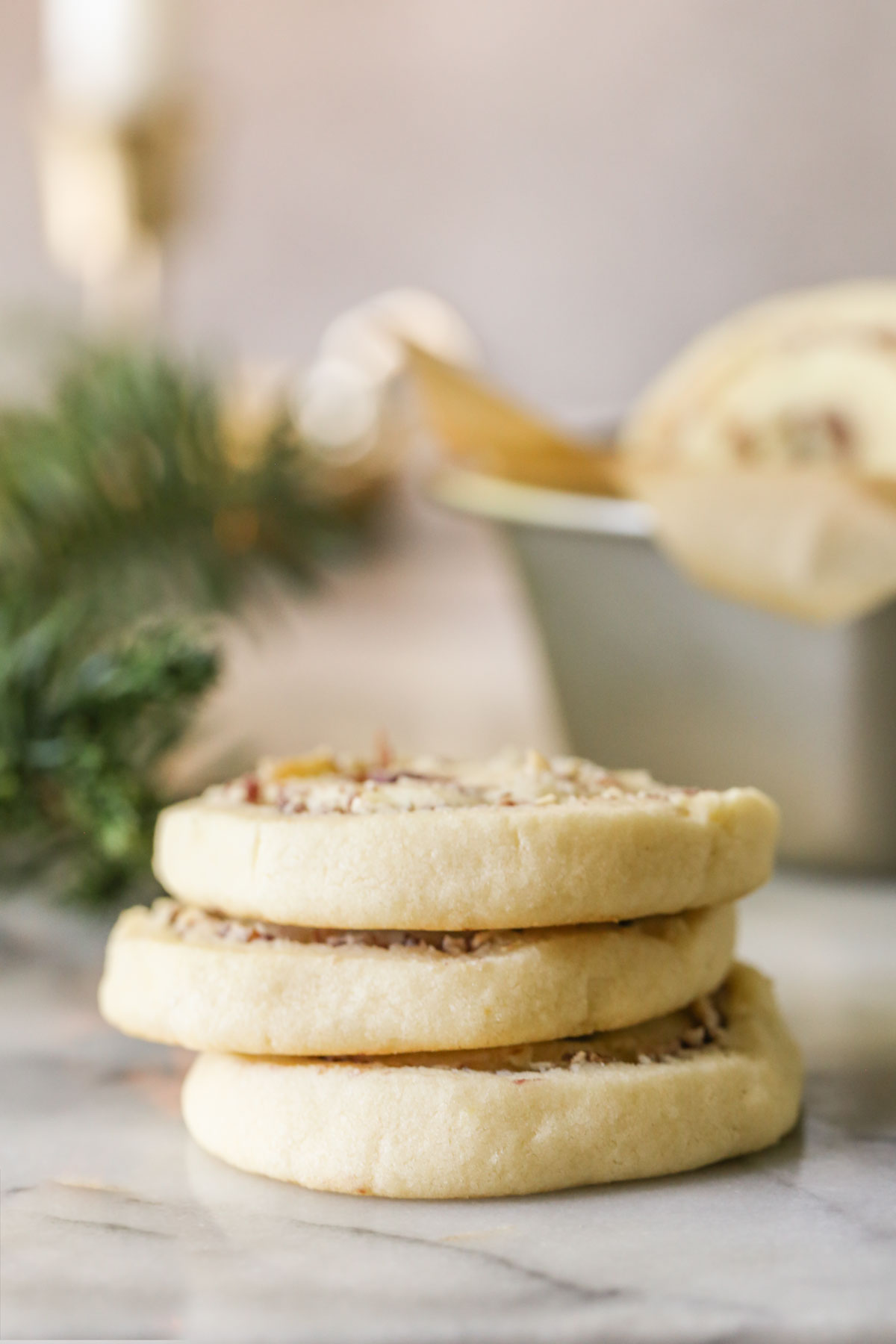 Three Raspberry Almond Pinwheels stacked, with more cookies in a mini loaf pan in the background, along with some greenery.