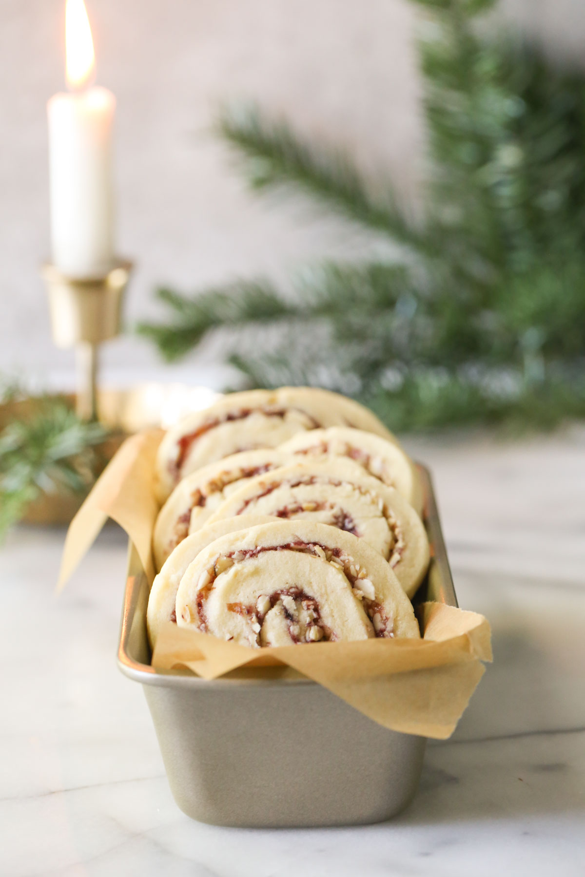 Raspberry Almond Pinwheels arranged in a parchment paper lined mini loaf pan, with a candle and greenery in the background.