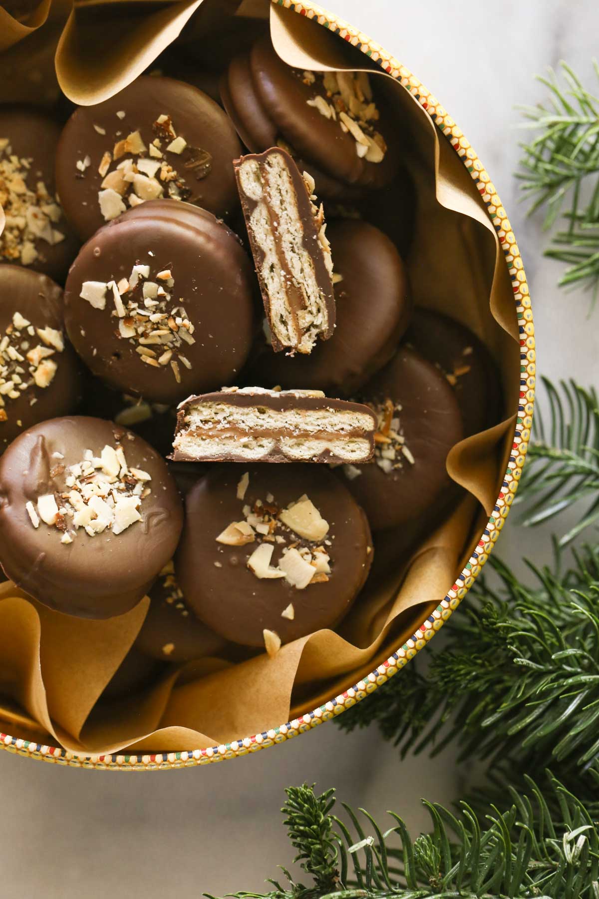 Overhead shot of Ritzy Rolo Cookies in a parchment paper lined cookie tin, with one cookie cut in half showing the inside layers of the cookie.