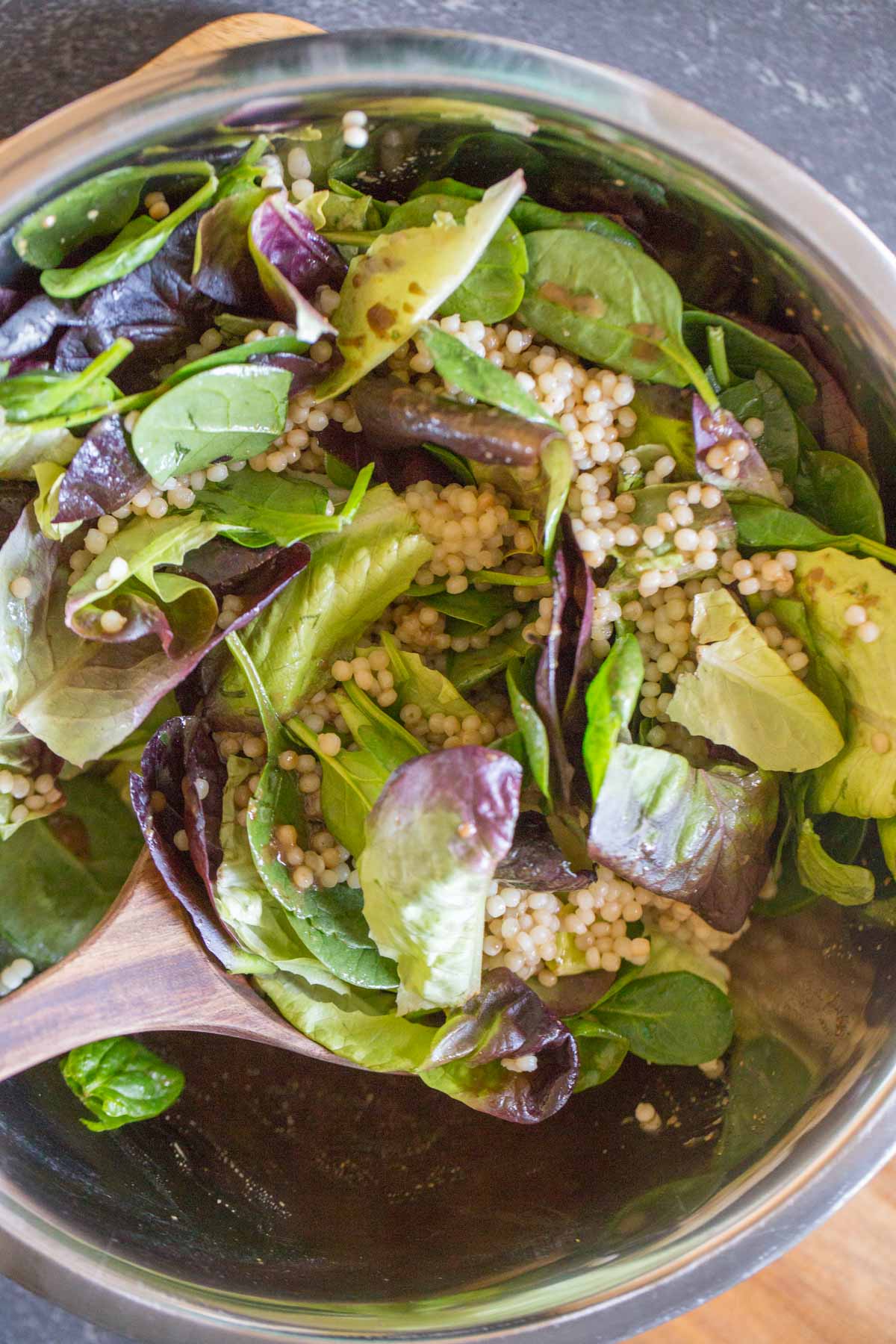 Overhead shot of a mixing bowl of the Couscous Salad with a wooden spoon in it. 