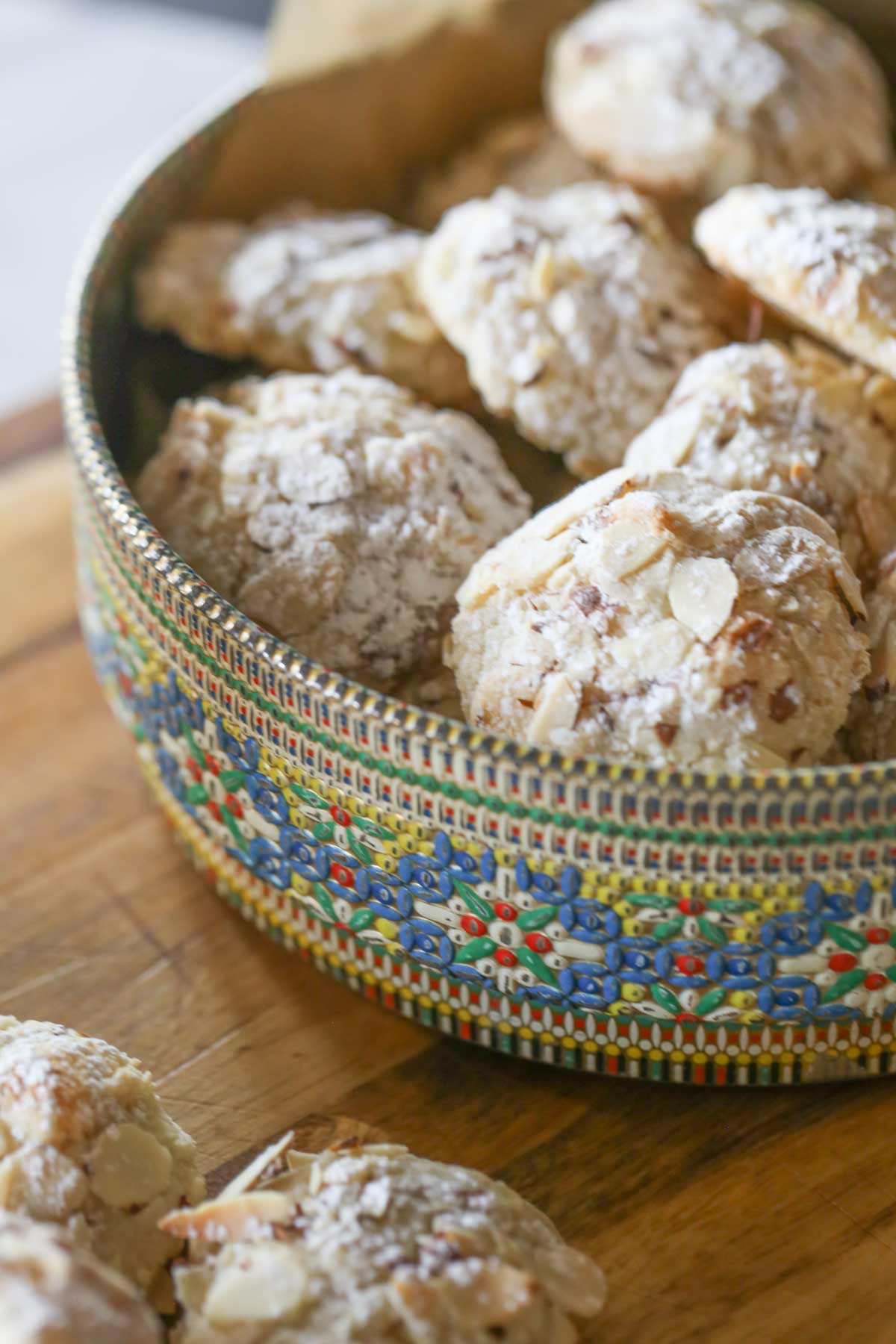 Almond Paste Cookies in a cookie tin on a wood cutting board, with more Almond Paste Cookies next to the tin. 