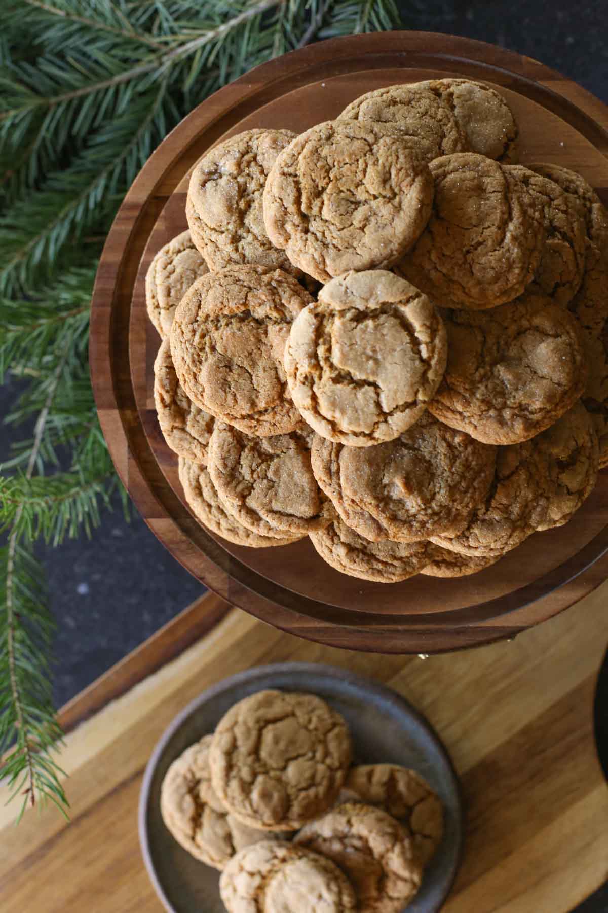 Overhead shot of Sourdough Ginger Molasses Cookies arranged on a wood cake stand, with more cookies on a plate below the cake stand. 