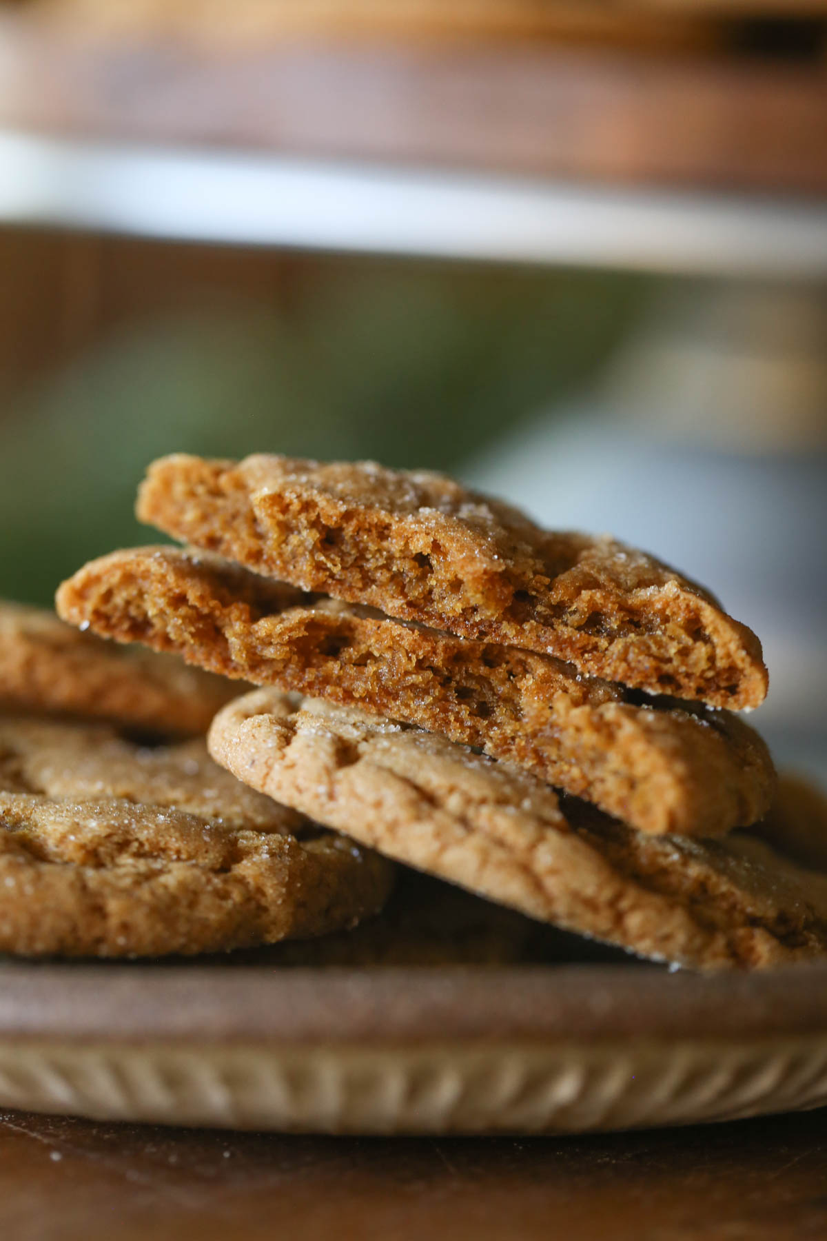 Close up shot of Sourdough Ginger Molasses Cookies on a plate, with one cookie broken in half showing the inside texture.  