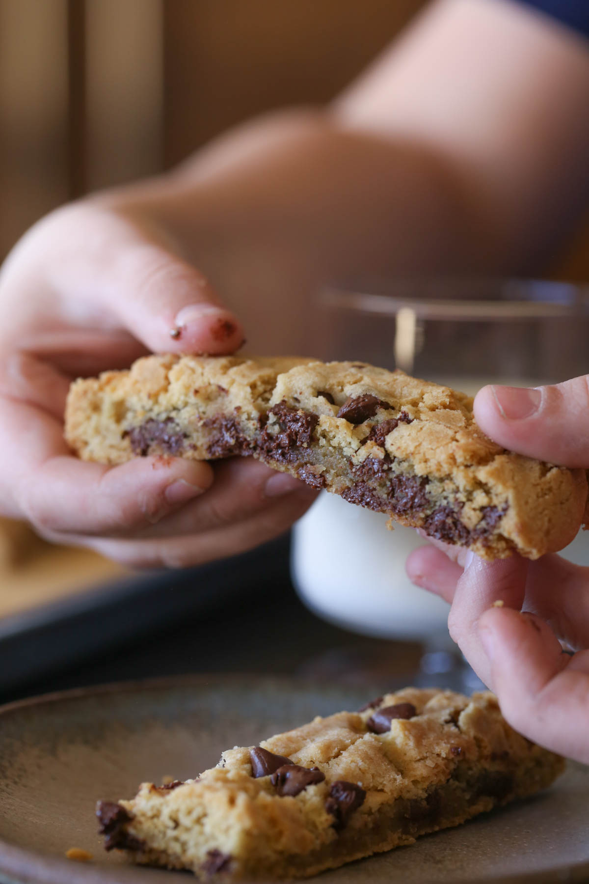 Hands holding a piece of a Chocolate Chip Cookie Stick ,showing a cross-section of melted chocolate chips and baked cookie dough.