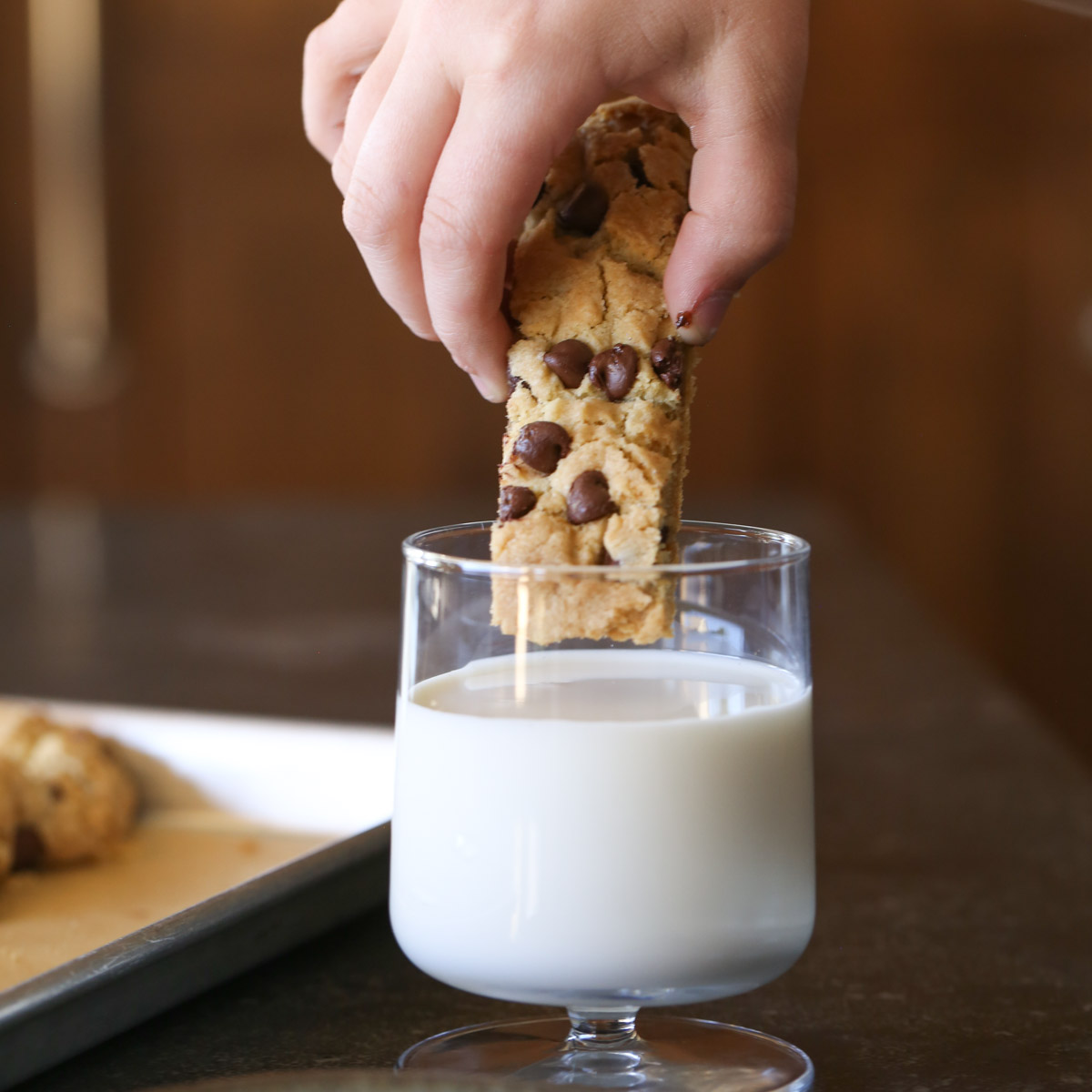 A hand dipping a Chocolate Chip Cookie Stick into a glass of milk.